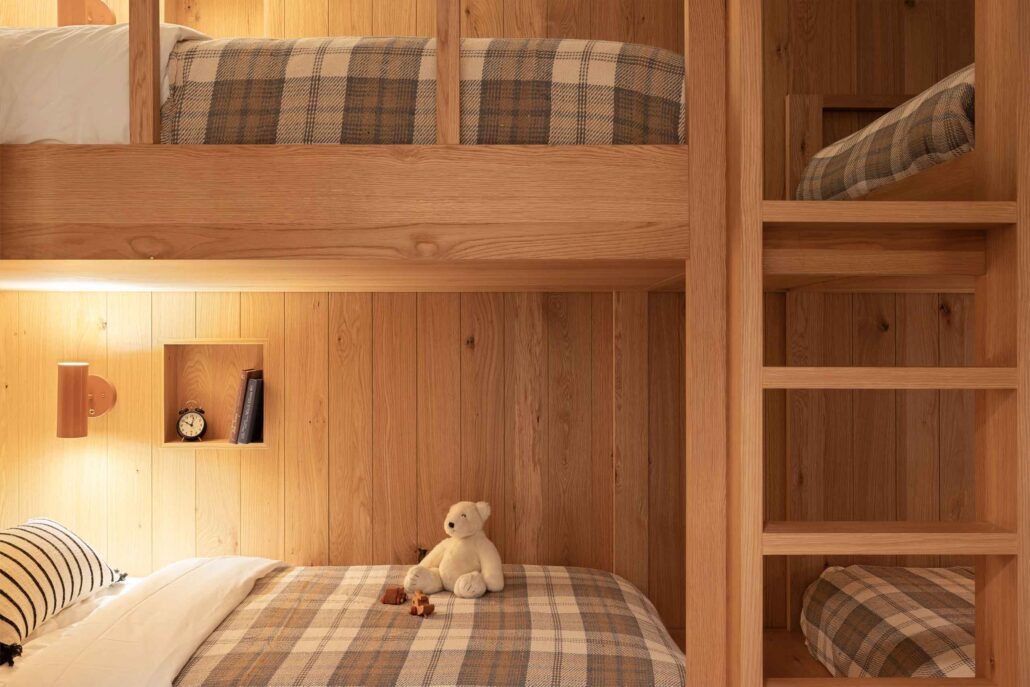 Detail of custom oak bunk beds with integrated shelving and warm ambient lighting.