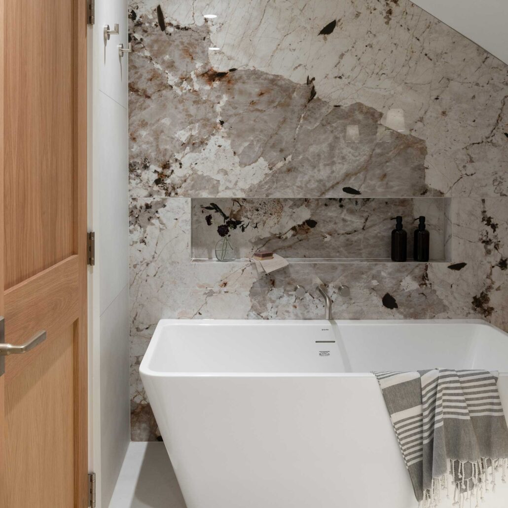 Luxury bathroom with dramatic natural stone tile, brushed brass shower enclosure, and freestanding tub.