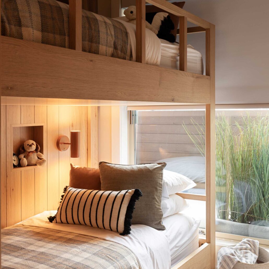 Custom built white oak bunk beds with integrated wall lighting, wood paneling, and warm contemporary styling for a mountain home.